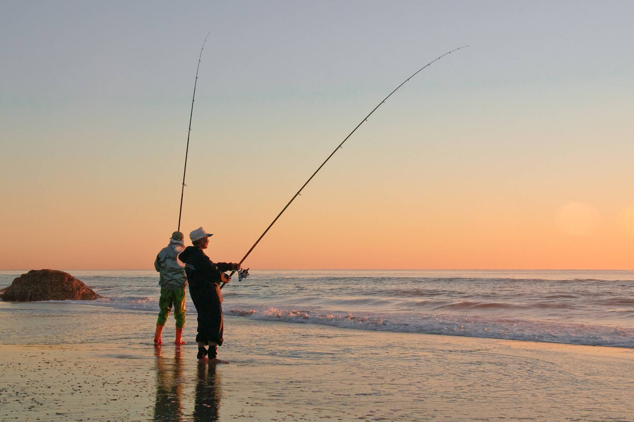 Two anglers casting into ocean waves
