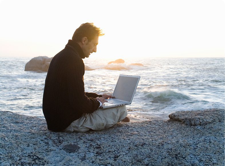 Man using laptop by the ocean