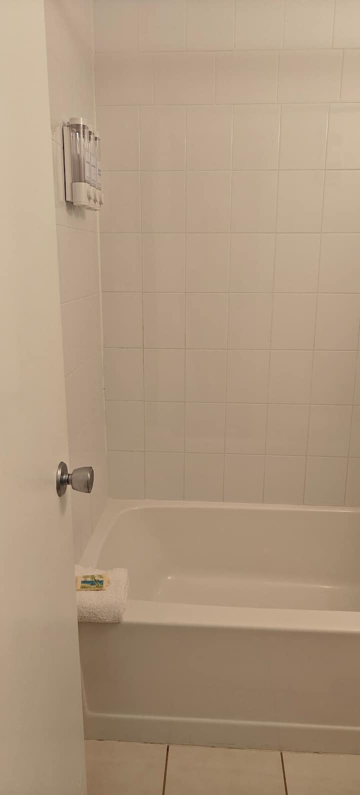 White bathtub with tiled wall and dispenser